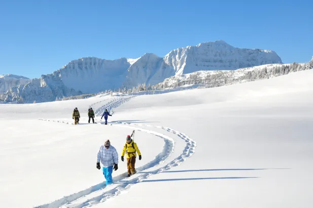 People exploring Sunshine Mountain on snowshoes with mountains behind