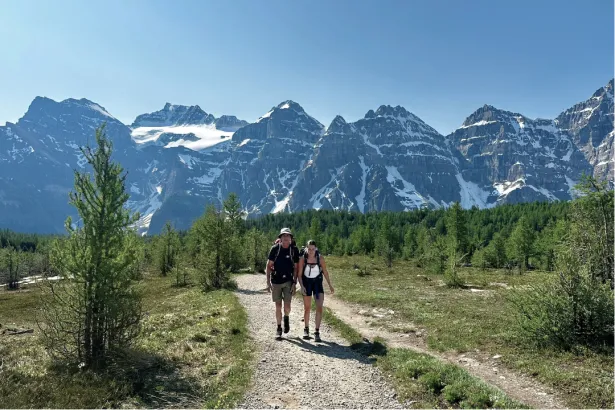 Two hikers on a summer trail at Moraine Lake with snow-capped Rocky Mountains in the background