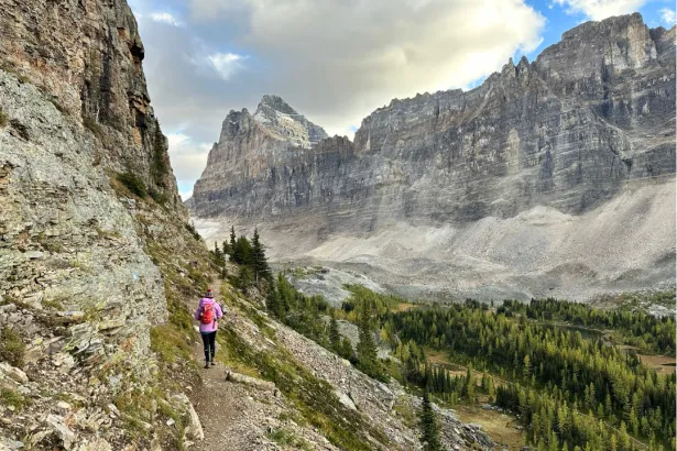 Hiker on a mountainside trail overlooking the valley on Lake O’Hara Tour with surrounding peaks in Yoho National Park, Canadian Rockies