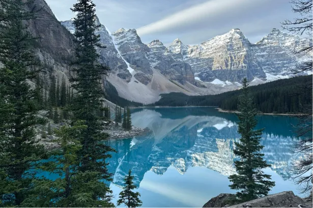 Scenic view of Moraine Lake with still waters reflecting towering mountains and pine trees in Banff, Canada