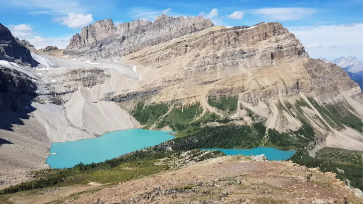 Glacial lake in Skoki Backcountry with crystal blue water, mountain peaks, visible glacier, and rocky moraine in Banff National Park