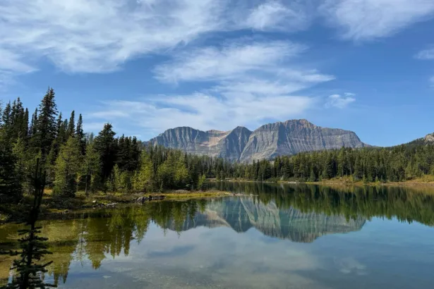 Scenic alpine lake in Sunshine Meadows with mirror-like reflection of mountain peaks and forested shoreline in Banff National Park