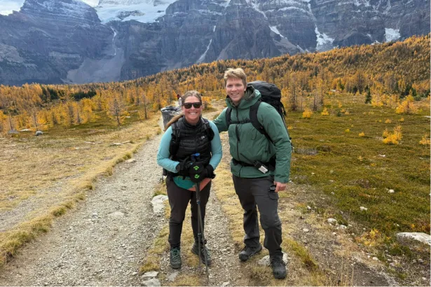 Hiker and White Mountain Adventures guide smiling on an autumn trail at Moraine Lake surrounded by golden larches
