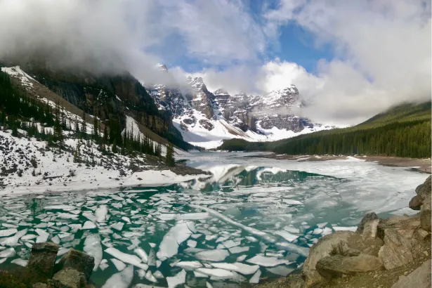Moraine Lake in spring showing melted ice, turquoise water, and snow-covered peaks in the Canadian Rockies