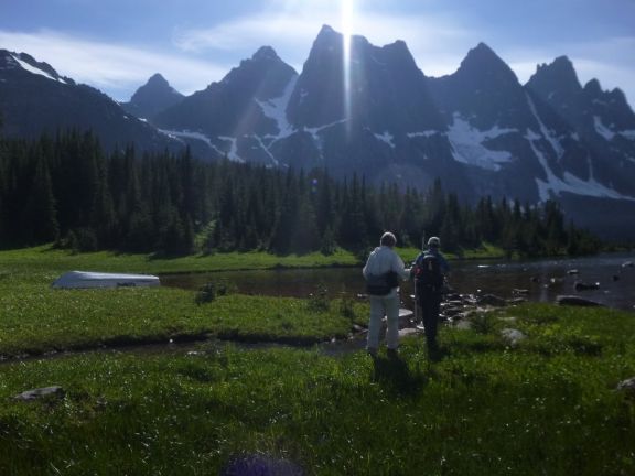 hikers take in view of small mountain lake in shadow of towering cliffs